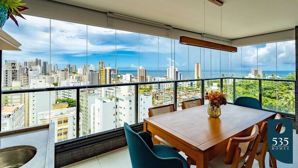 A modern dining area with a city view, a wooden table, and chairs. - Beautiful and cozy with a panoramic view in Barra (Salvador)
