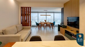 A modern living room with a sofa, dining table, chairs, and a TV. - Beautiful and cozy with a panoramic view in Barra (Salvador)