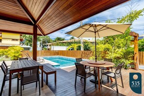 En udendørs terrasse med træmøbler, swimmingpool og et træhegn.