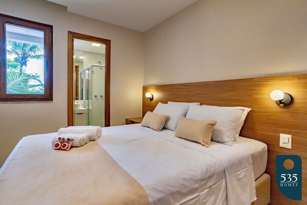En pænt redt seng med hvide sengetæpper, et træhovedgærde og to vægmonterede lamper.