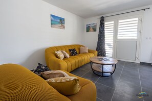 Un salón con un sofá color mostaza, una mesa de centro redonda y dos cuadros en la pared.