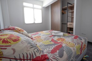 Un dormitorio con una cama con cubrecama floral, una ventana y un armario empotrado con espacio para colgar ropa.