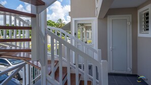 A staircase with white railings leading to a door, a view of parked cars, and a clear sky. - L'anse Plage. Situation Géographique Idéale (L'anse a l'âne)
