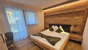 Ein hölzernes Bett mit Kopfteil, ein Stuhl und ein Fenster mit durchsichtigen Vorhängen.