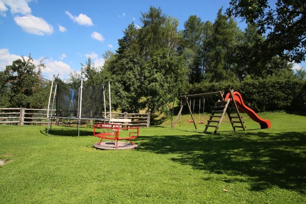A playground with a swing set and a slide, surrounded by a wooden fence and trees.
