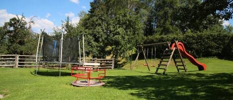 A playground with a swing set and a slide, surrounded by a wooden fence and trees.
