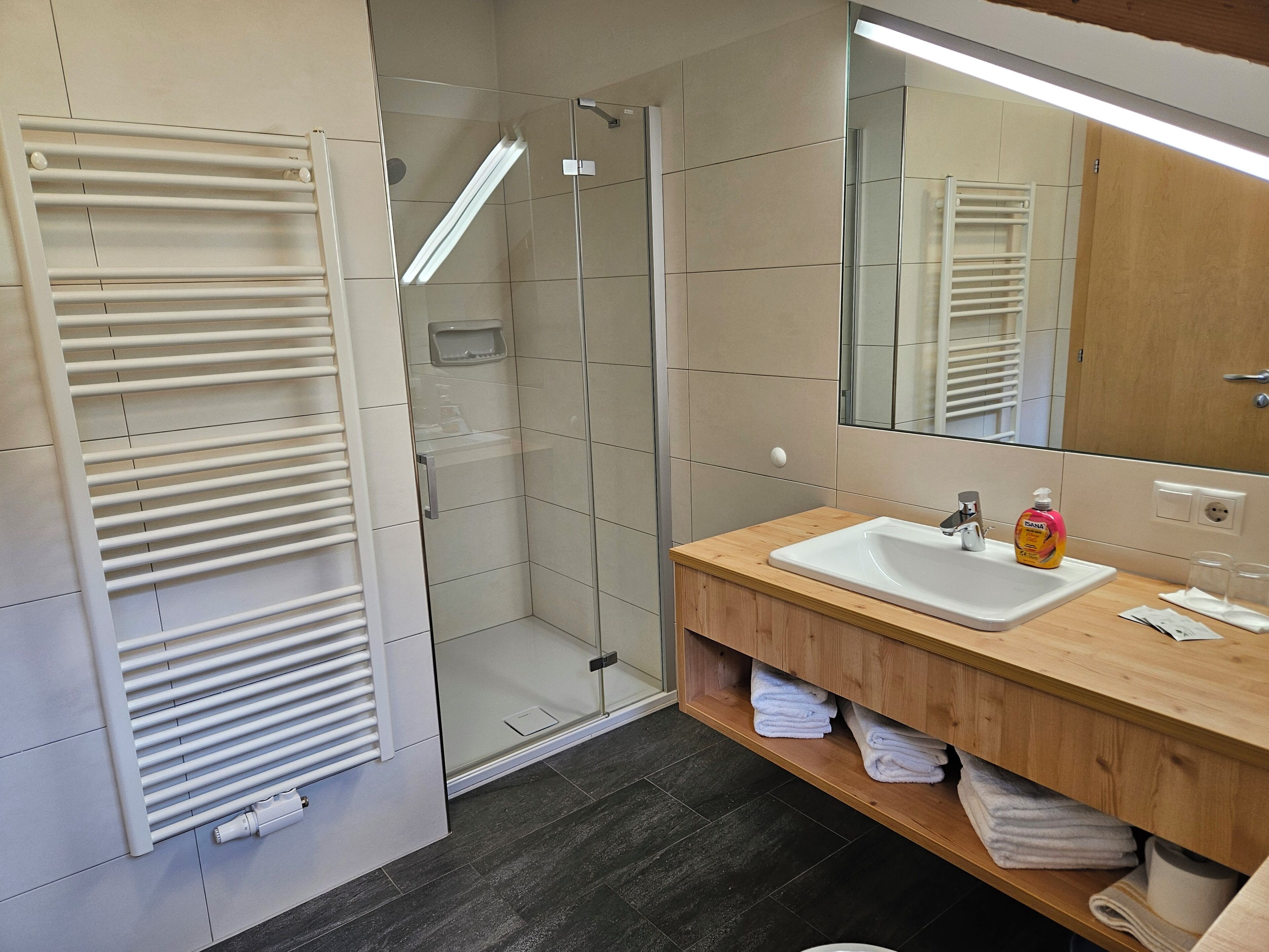 A modern bathroom with a glass-enclosed shower, a white sink, and a wooden vanity.