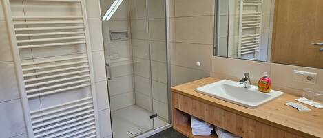 A modern bathroom with a glass-enclosed shower, a white sink, and a wooden vanity.
