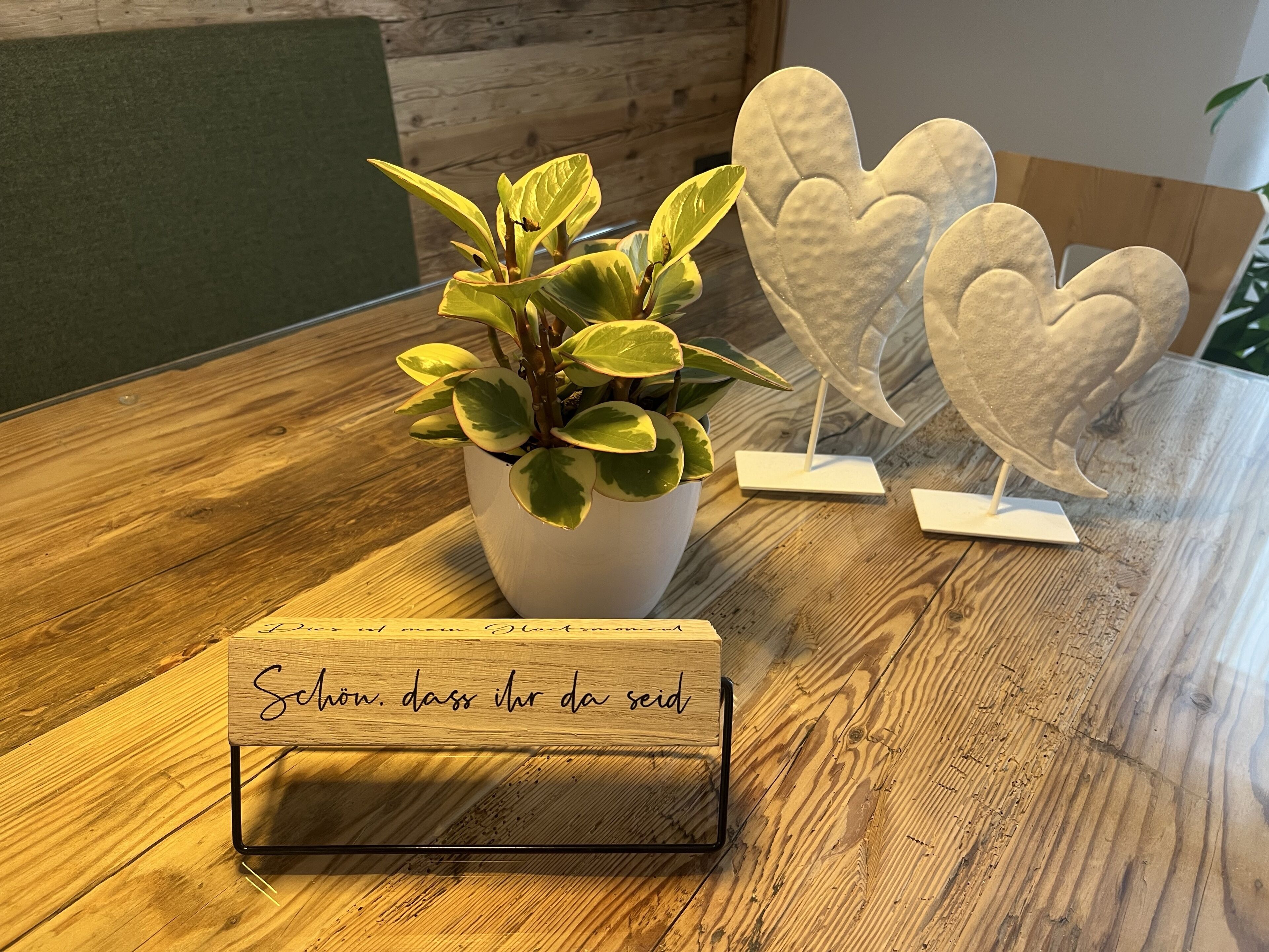 A wooden table with a potted plant, heart-shaped decorations, and a sign with text.