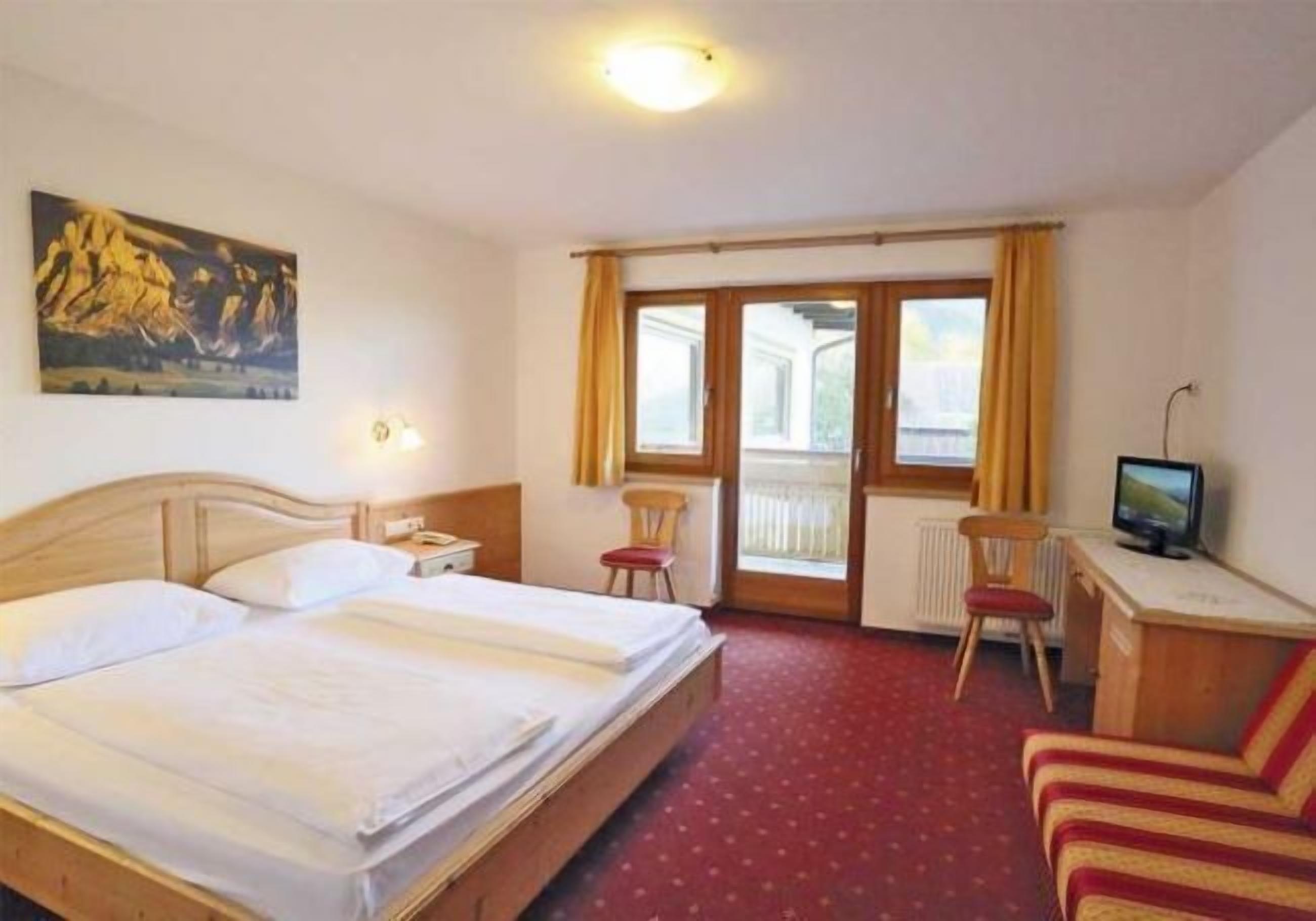 Una habitación de hotel con cama, escritorio, silla, televisión y un cuadro en la pared.