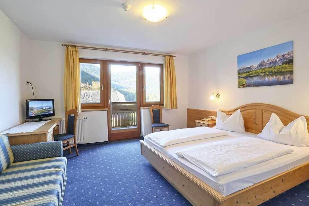 Habitación de hotel con cama, escritorio con computadora, silla, ventana con cortinas y un cuadro en la pared.