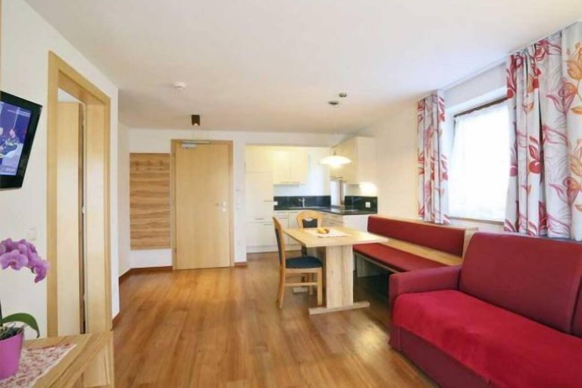 Un espacio habitable compacto con kitchenette, zona de comedor y sofá rojo.