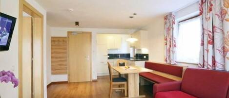 Un espacio habitable compacto con kitchenette, zona de comedor y sofá rojo.