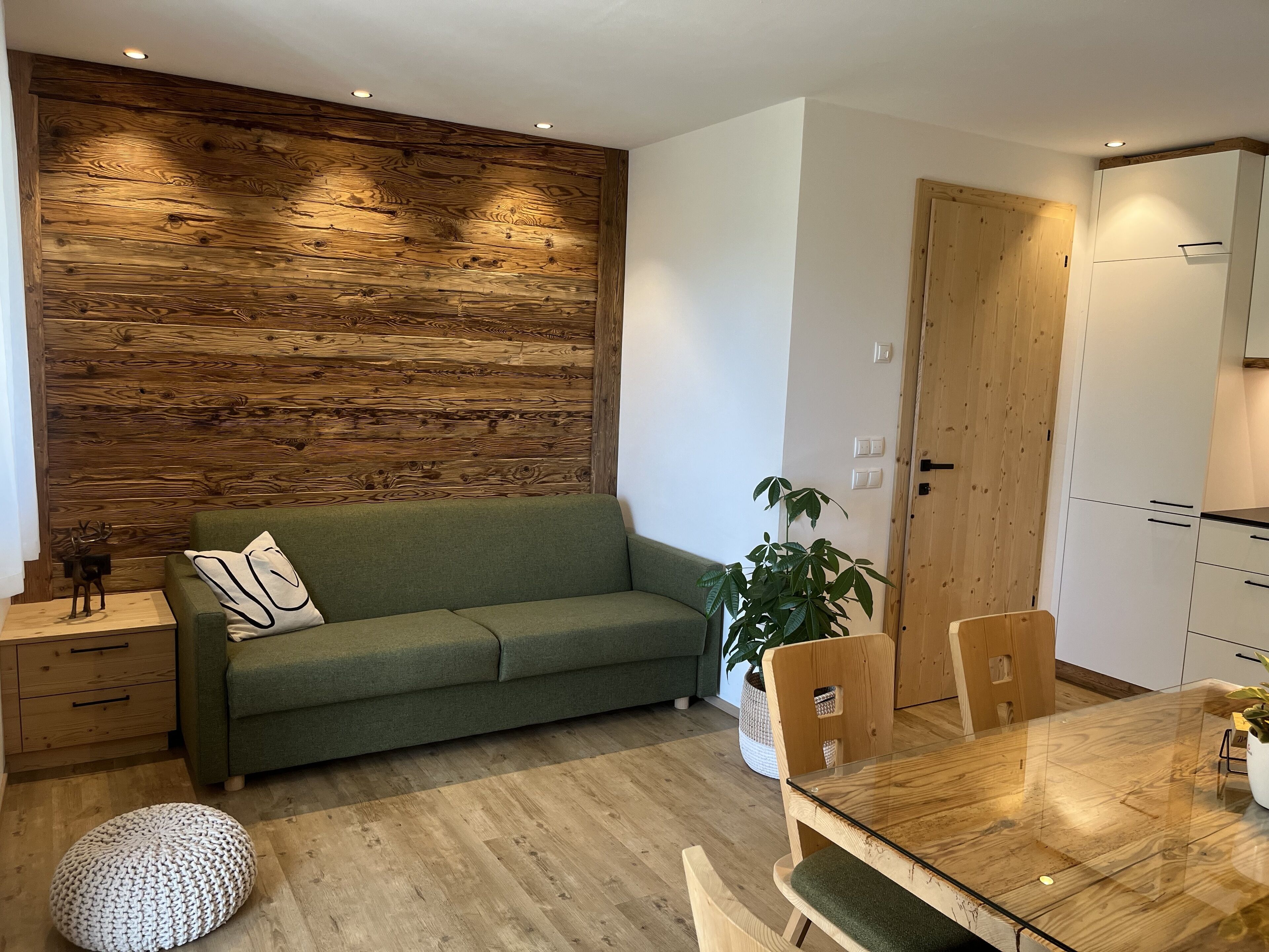 A modern living space with a wooden accent wall, a green sofa, a dining table with chairs, and a wooden cabinet.