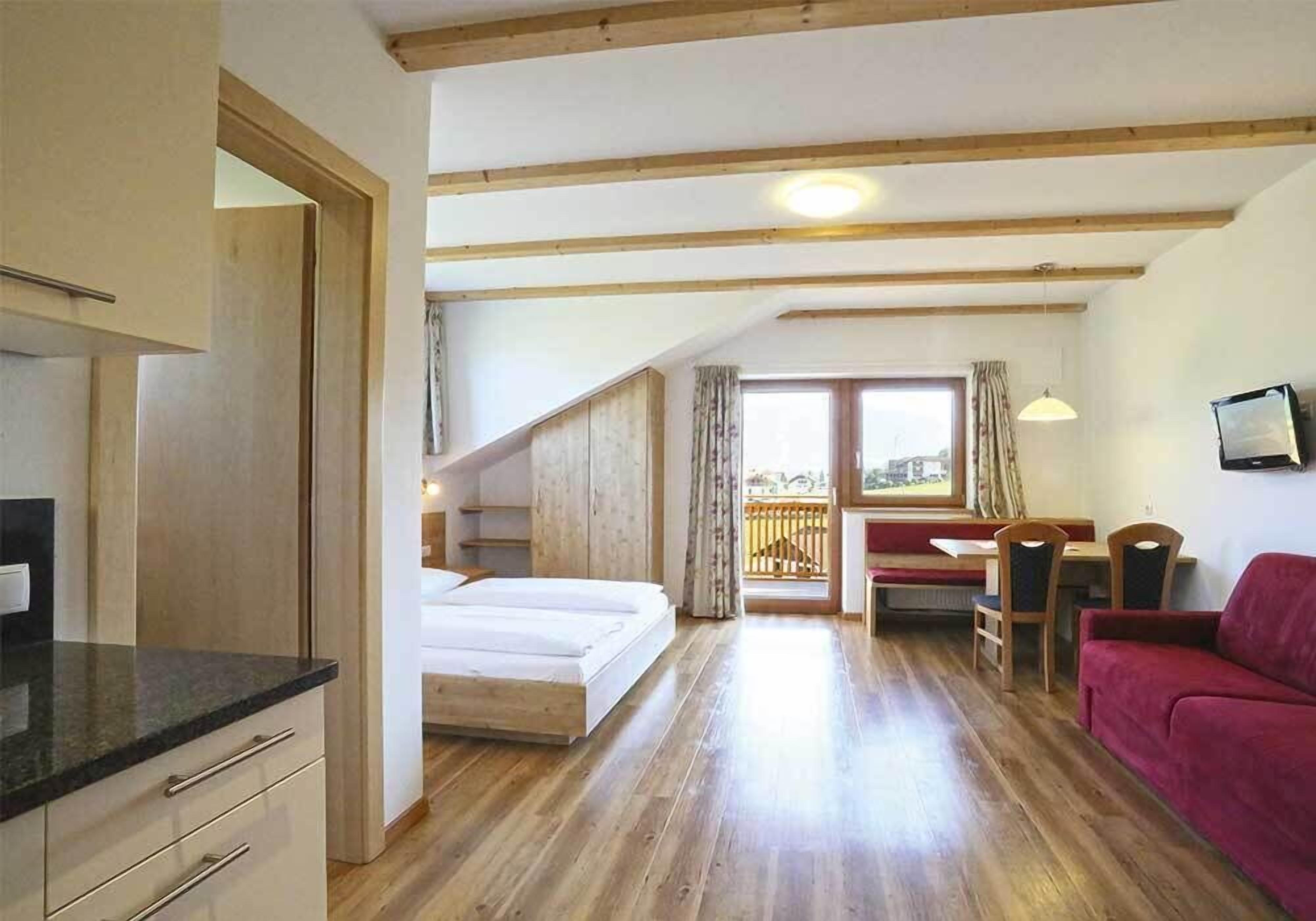 Une chambre avec un lit, un bureau, un canapé rouge et un balcon avec vue.