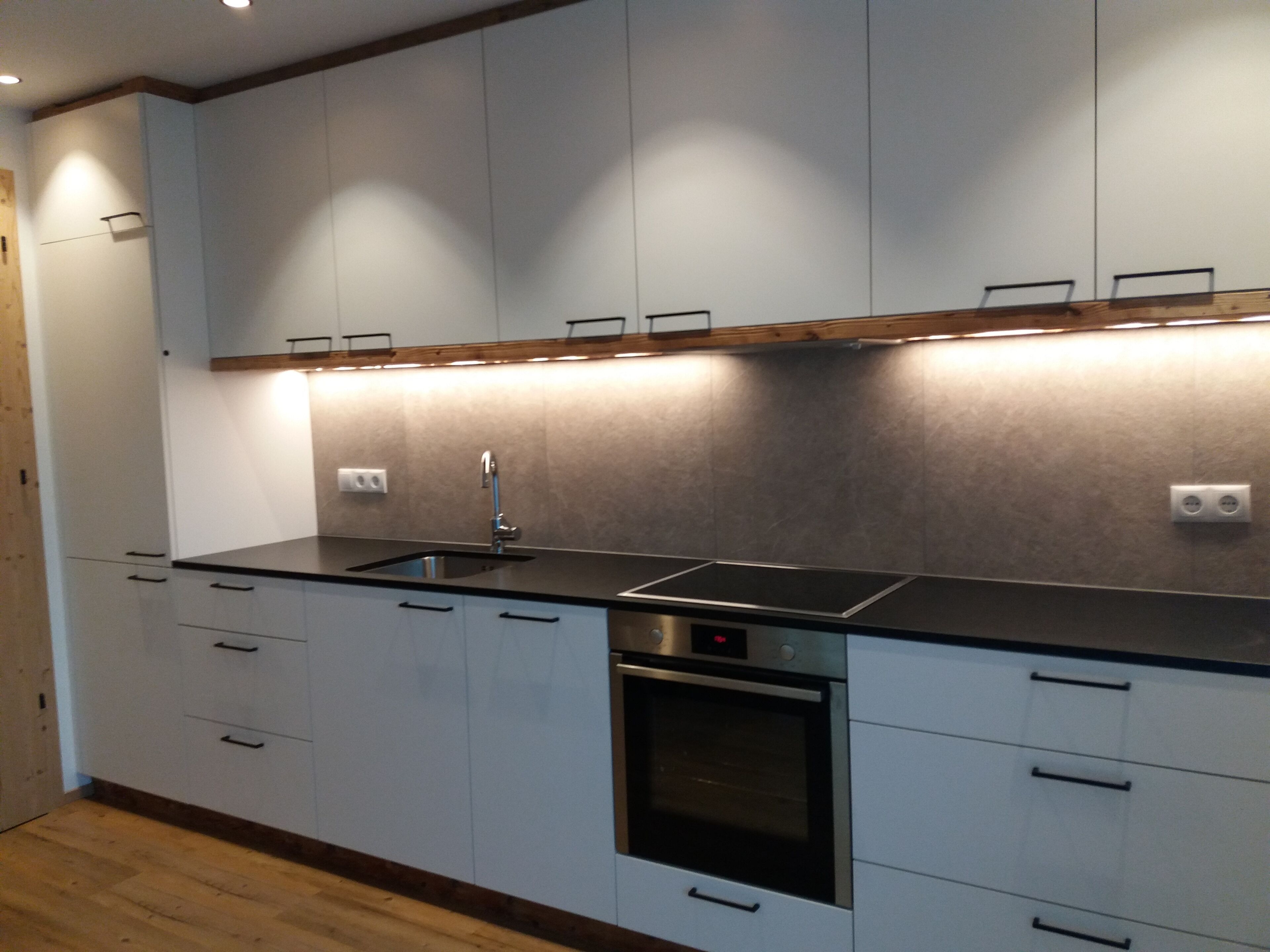 A modern kitchen with white cabinets, a stainless steel sink, and a built-in oven.