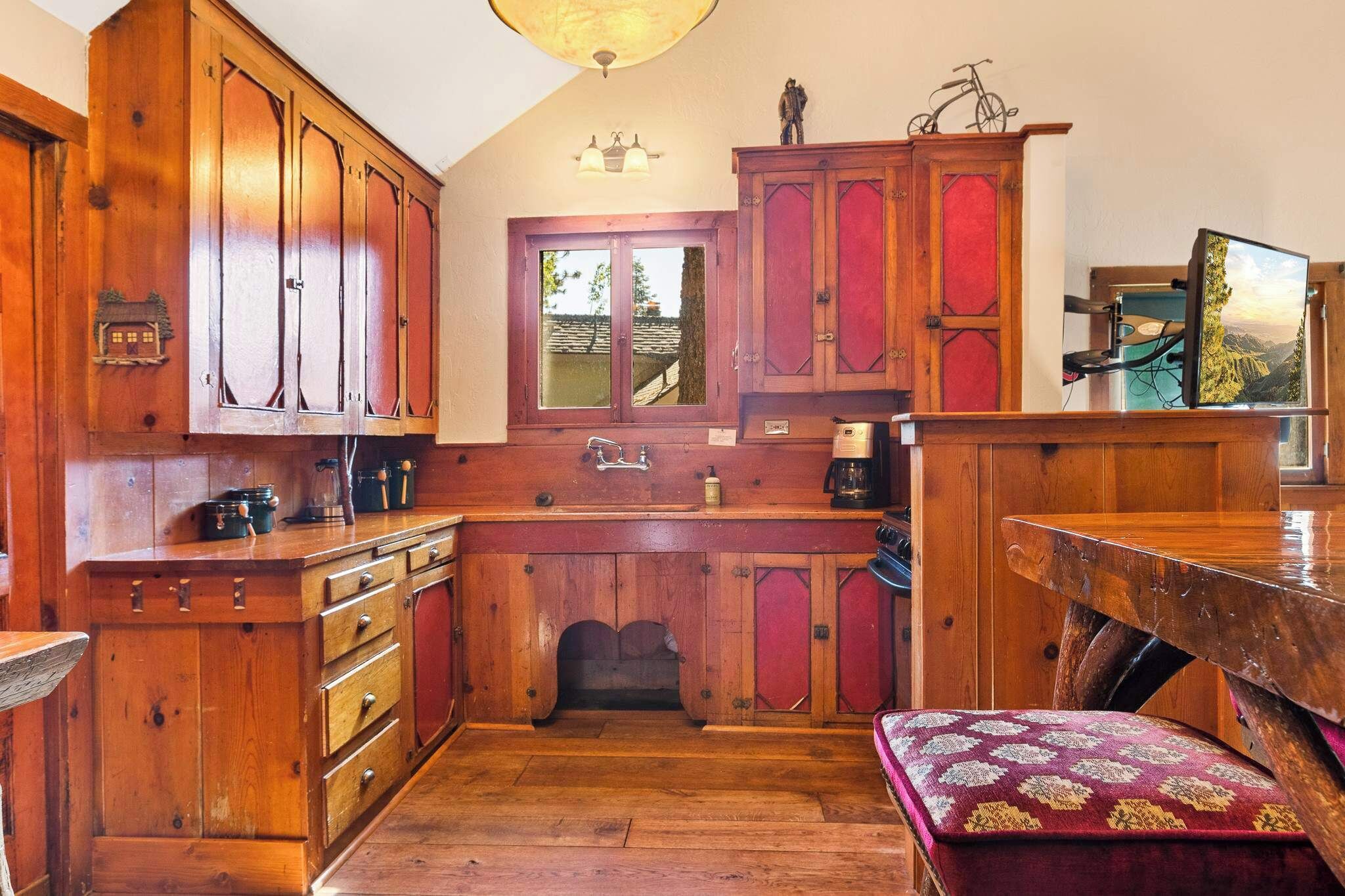 A wooden kitchen with cabinets, a window, and a table with a red cushioned bench.