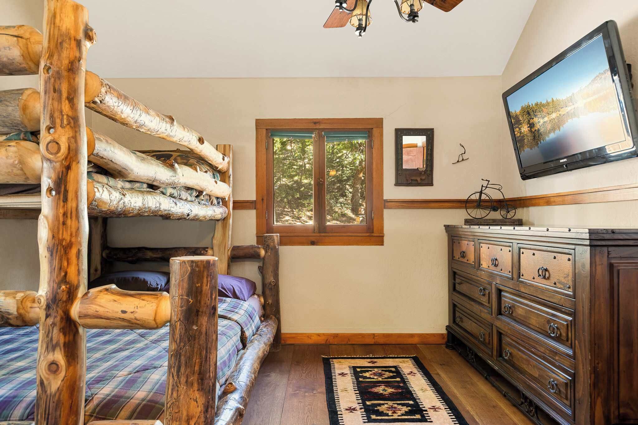 A rustic bedroom with a bunk bed, wooden dresser, and a television on the wall.