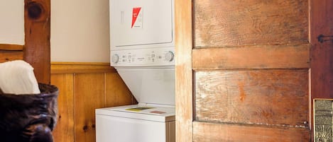 A laundry room with a white washing machine and dryer, wooden walls, and a wooden door.