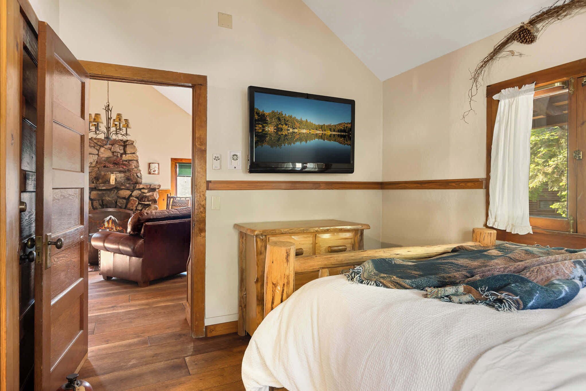 A bedroom with a bed, a wooden dresser, a television on the wall, and a stone fireplace.