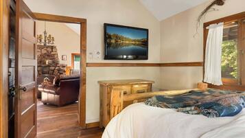 A bedroom with a bed, a wooden dresser, a television on the wall, and a stone fireplace.