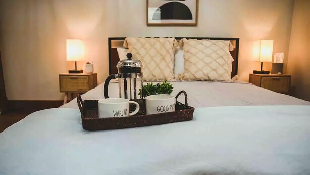 A neatly made bed with a tray of two white mugs, one labeled "WAKE UP" and the other "GOOD MORNING," and a coffee pot. - Keuka Village House, Penn Yan
 (Penn Yan)