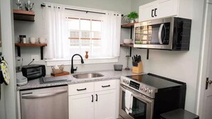 A compact kitchen with white cabinets, a built-in microwave, a stove, and a sink. - Keuka Village House, Penn Yan
 (Penn Yan)