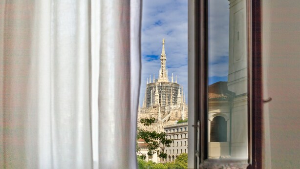 Blick auf ein historisches Gebäude mit aufwendiger Architektur, sichtbar durch ein Fenster mit Vorhängen.