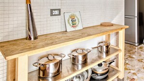 Eine Küche mit einer Holzausziehtheke, drei Edelstahl-Töpfen, einer Reibe und einem gerahmten Bild an der Wand.