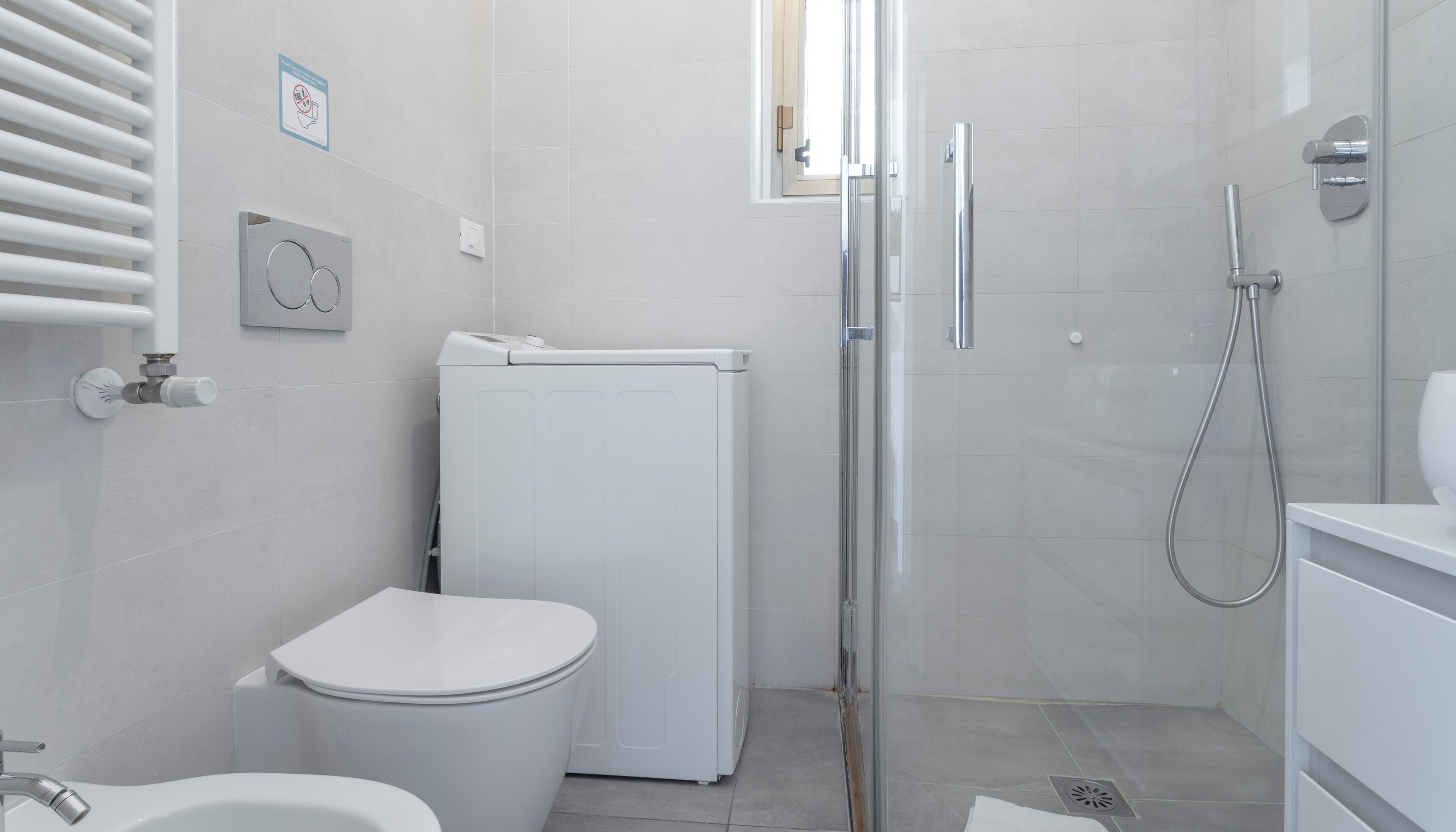 A small, modern bathroom with a toilet, a washing machine, and a shower.