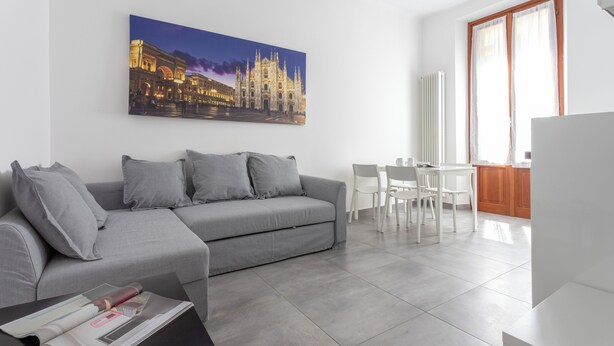 Ein modernes Wohnzimmer mit einem grauen Sofa, einem Esstisch mit Stühlen und einem großen Fenster.