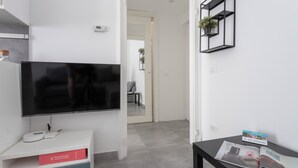 Ein modernes Wohnzimmer mit einem Flachbildfernseher, einer weißen Konsole mit einer roten Gebrauchsanweisung und einem schwarzen Beistelltisch mit einer Zeitschrift.