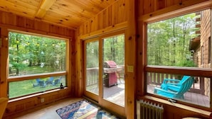 A wooden cabin with large windows, a deck with blue chairs, and a barbecue grill outside. - Log Cabin w/  Full Garage, FirePit, BBQ, cozy gas heat Stove (Pocono Lake)
