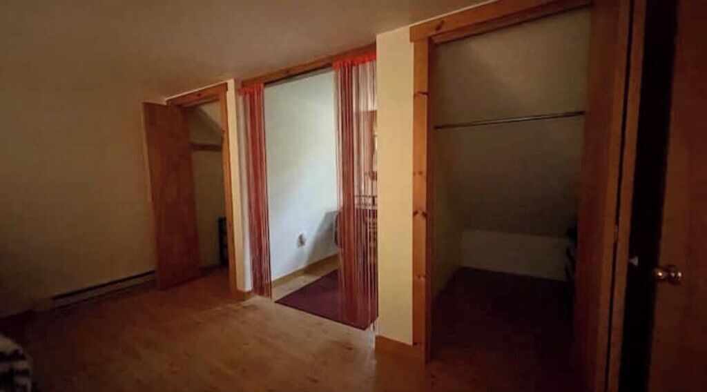 Ein Zimmer mit Holzboden, einer Tür mit rotem Vorhang und einem sichtbaren Kleiderschrank.