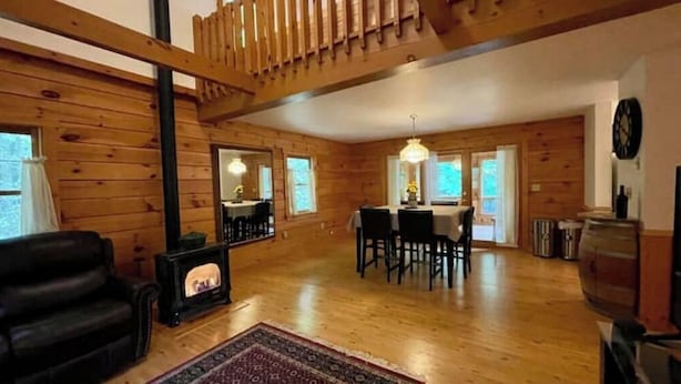 A wooden interior with a fireplace, dining area, and a staircase. - Log Cabin w/  Full Garage, FirePit, BBQ, cozy gas heat Stove (Pocono Lake)