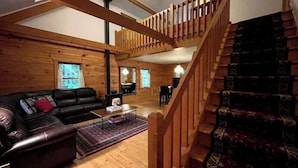 A cozy living room with a wooden staircase, a leather sofa, and a dining area. - Log Cabin w/  Full Garage, FirePit, BBQ, cozy gas heat Stove (Pocono Lake)