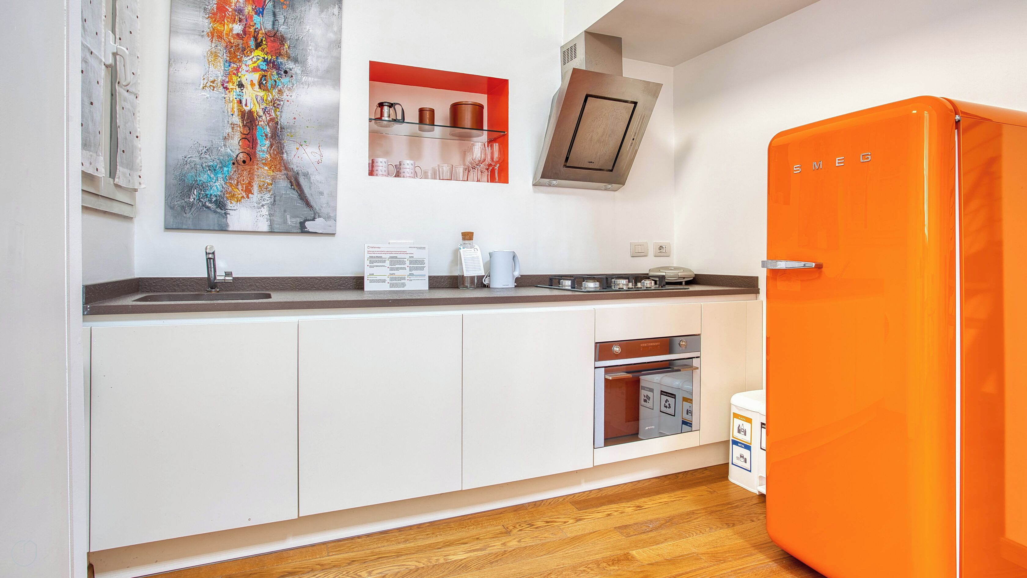 A modern kitchen with white cabinets, a stainless steel sink, and an orange refrigerator.