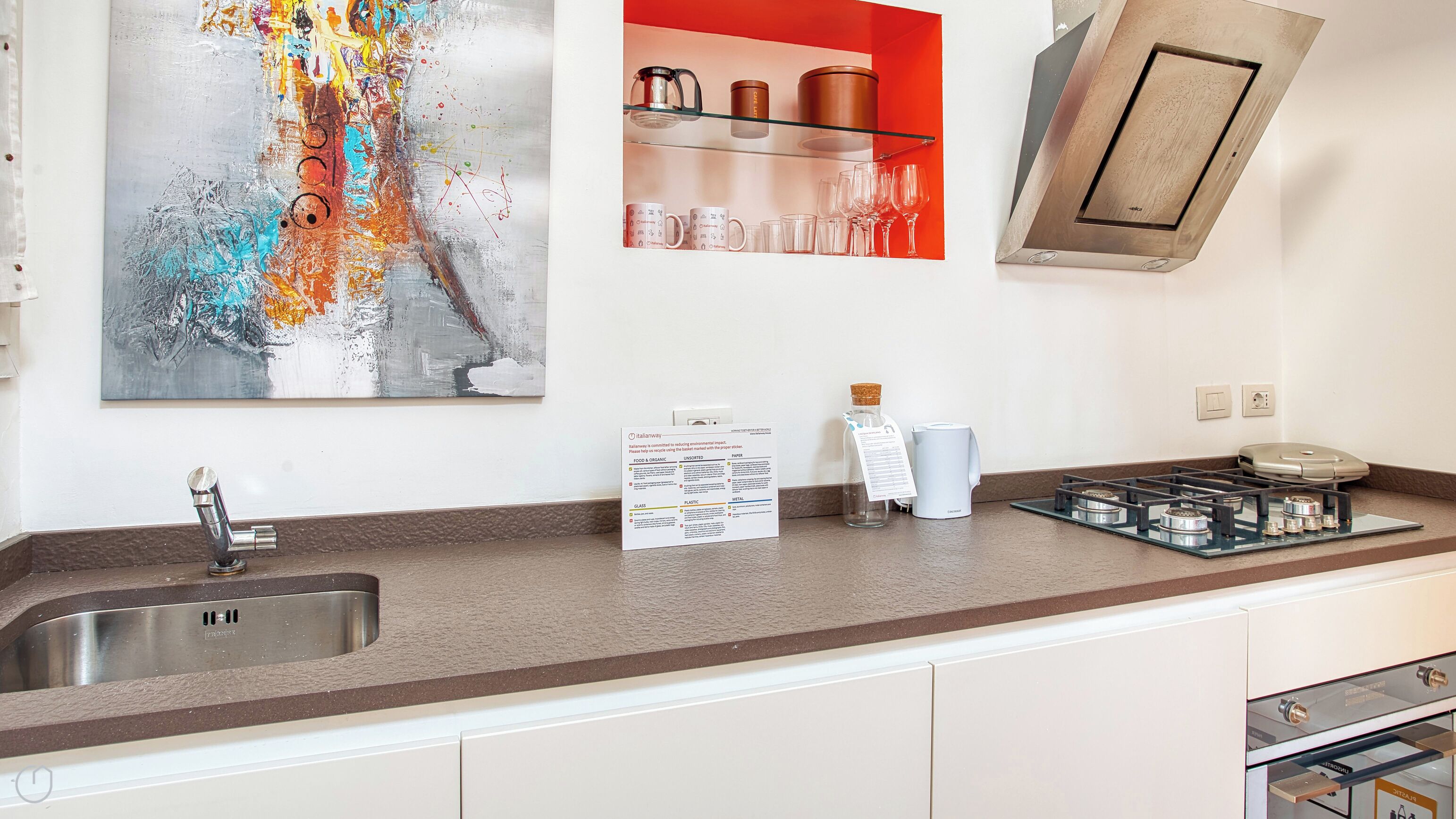 Una cucina moderna con lavello in acciaio inox, una moka in vetro e una caffettiera sul piano di lavoro.
