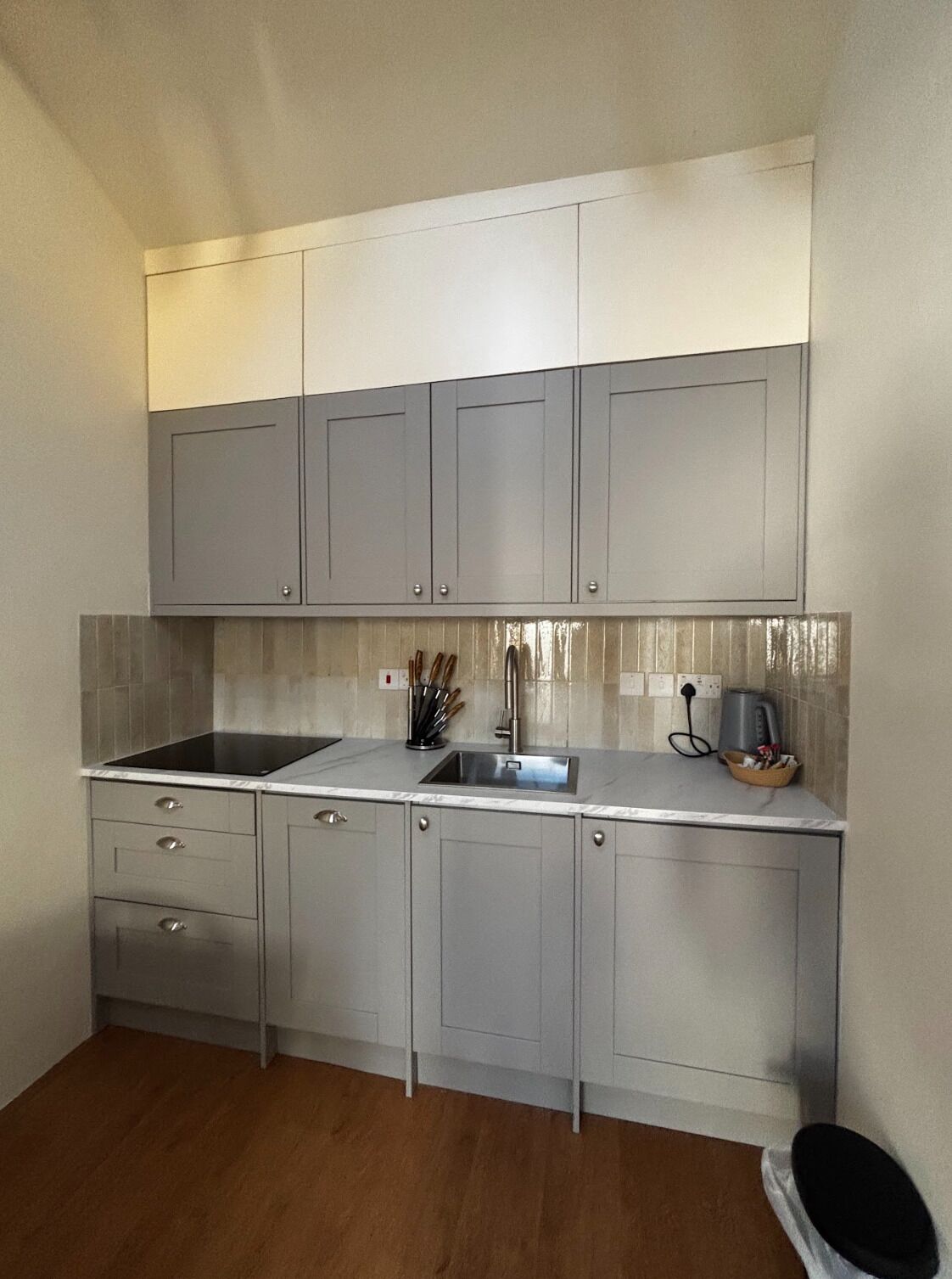 A compact kitchen with grey cabinets, a black countertop, and a stainless steel sink.