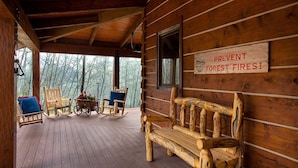 A wooden cabin with a porch, rocking chairs, a bench, and a sign warning against forest fires.