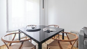 A modern dining area with a glass table, four wicker chairs, a black table base, and a window with sheer curtains. - Italianway - Palestrina 31 (Milan)