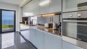 A modern kitchen with a large island, built-in appliances, and a view of the sea. - Mango (Funchal)