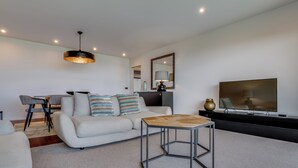 A modern living room with a sofa, a coffee table, a TV, and a dining area with chairs. - Mango (Funchal)