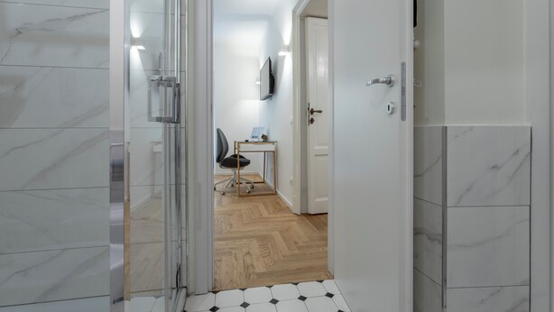 A hallway with a glass door, a wooden floor, a desk with a chair, and a mounted TV. - Italianway - Pontaccio 2 (Milan)