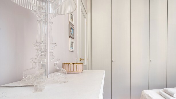 Une coiffeuse blanche, surmontée d’un lustre en verre transparent, avec un miroir à cadre doré et une serviette blanche posée sur une table.