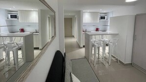A modern kitchen with white cabinetry, a microwave, and a red kettle. There is a dining area with white chairs and a table. - Studio In San Telmo- Paseo De La Cisterna- 529 (Buenos Aires)