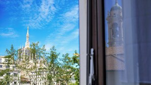 A view of a historic building with a tall spire and a clock tower, surrounded by trees and other buildings. - Italianway - Merlo 1/3 C (Milan)
