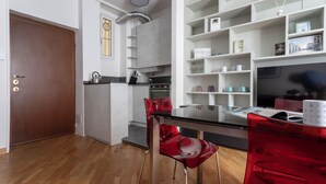 Cozinha moderna com armários brancos, porta de madeira e área de jantar com mesa de vidro e cadeiras vermelhas.