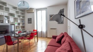 Uma sala de estar moderna com um sofá vermelho, uma mesa de jantar de vidro com cadeiras vermelhas, uma TV grande e uma luminária no teto.