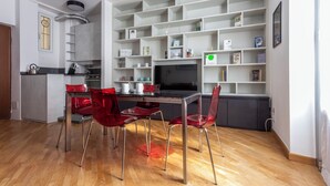 Cozinha moderna com área de refeições, com mesa de vidro e cadeiras vermelhas, estante embutida e bancada na cozinha.